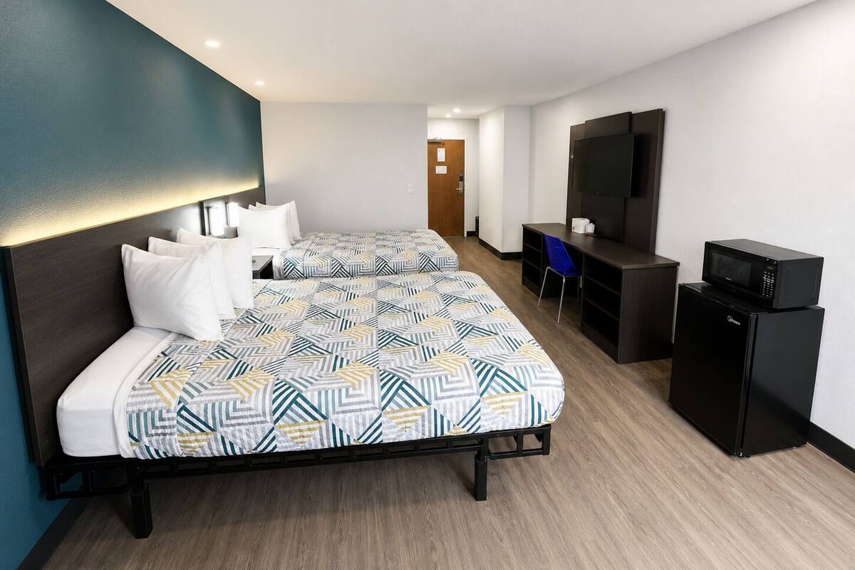 A hotel room with two beds, a desk, a chair, a TV, and a microwave.