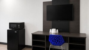 Una habitación moderna con televisor de pantalla plana montado en la pared, un refrigerador negro, una silla azul y un escritorio de madera.