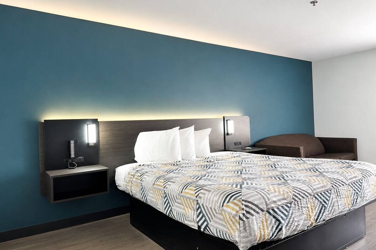 A modern hotel room with a large bed, a bedside table with a lamp, and a built-in shelf.