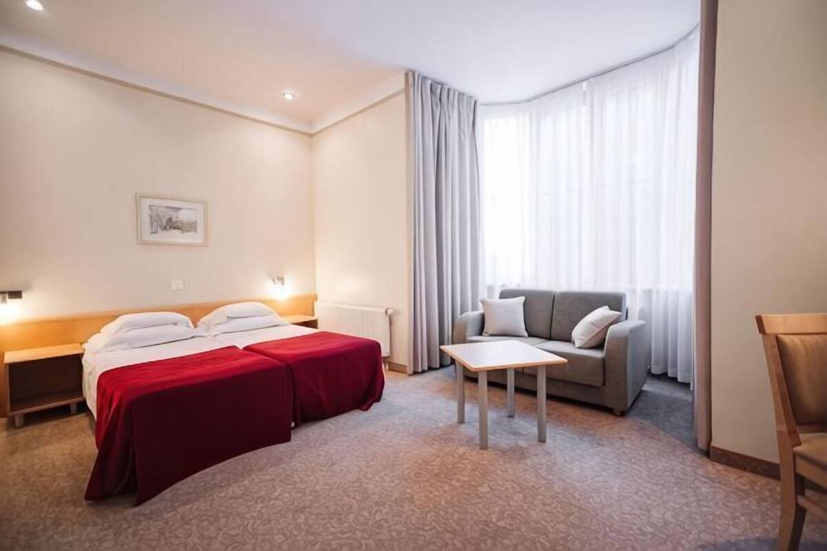 Ein Hotelzimmer mit einem Bett, zwei Nachttischen, einem Sofa, einem kleinen Tisch und einem Fenster mit Vorhängen.