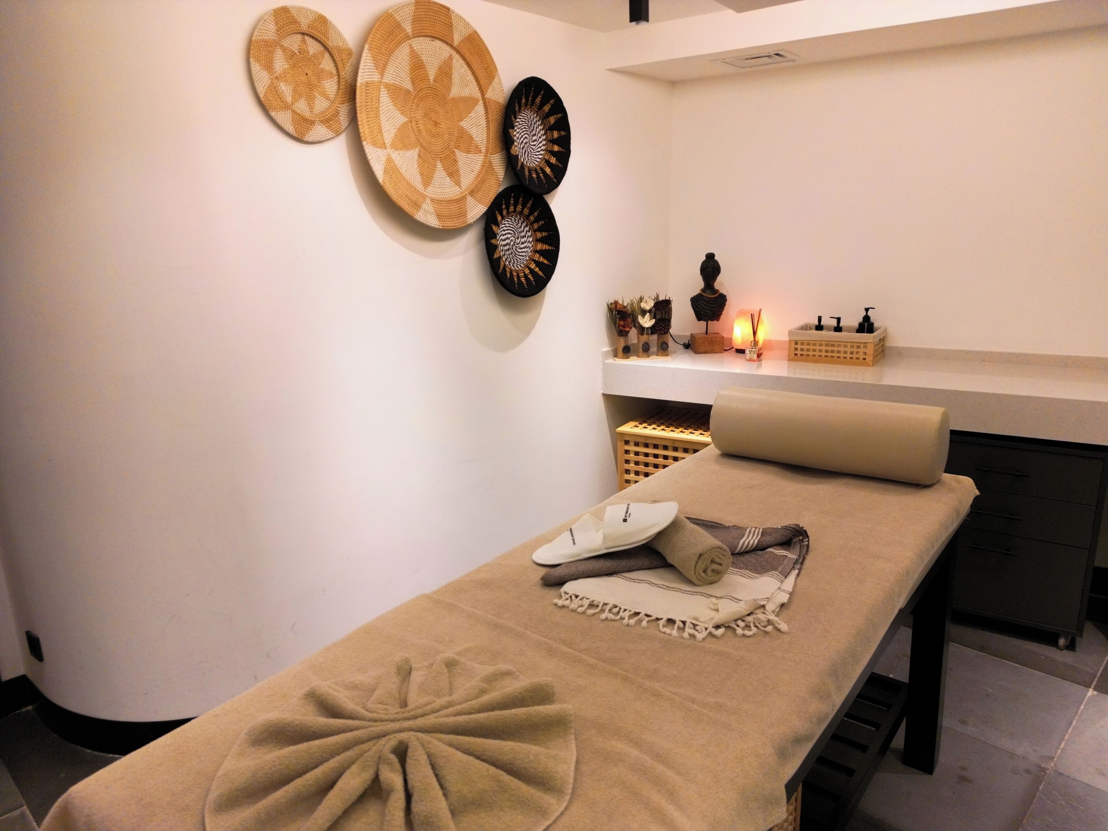 Ein Spa-Raum mit Massagetisch, einer Wandablage mit Dekoration und einer kleinen Ablage für Pflegeprodukte.