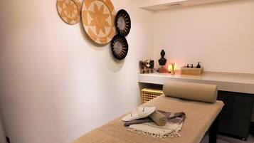 Ein Spa-Raum mit Massagetisch, einer Wandablage mit Dekoration und einer kleinen Ablage für Pflegeprodukte.