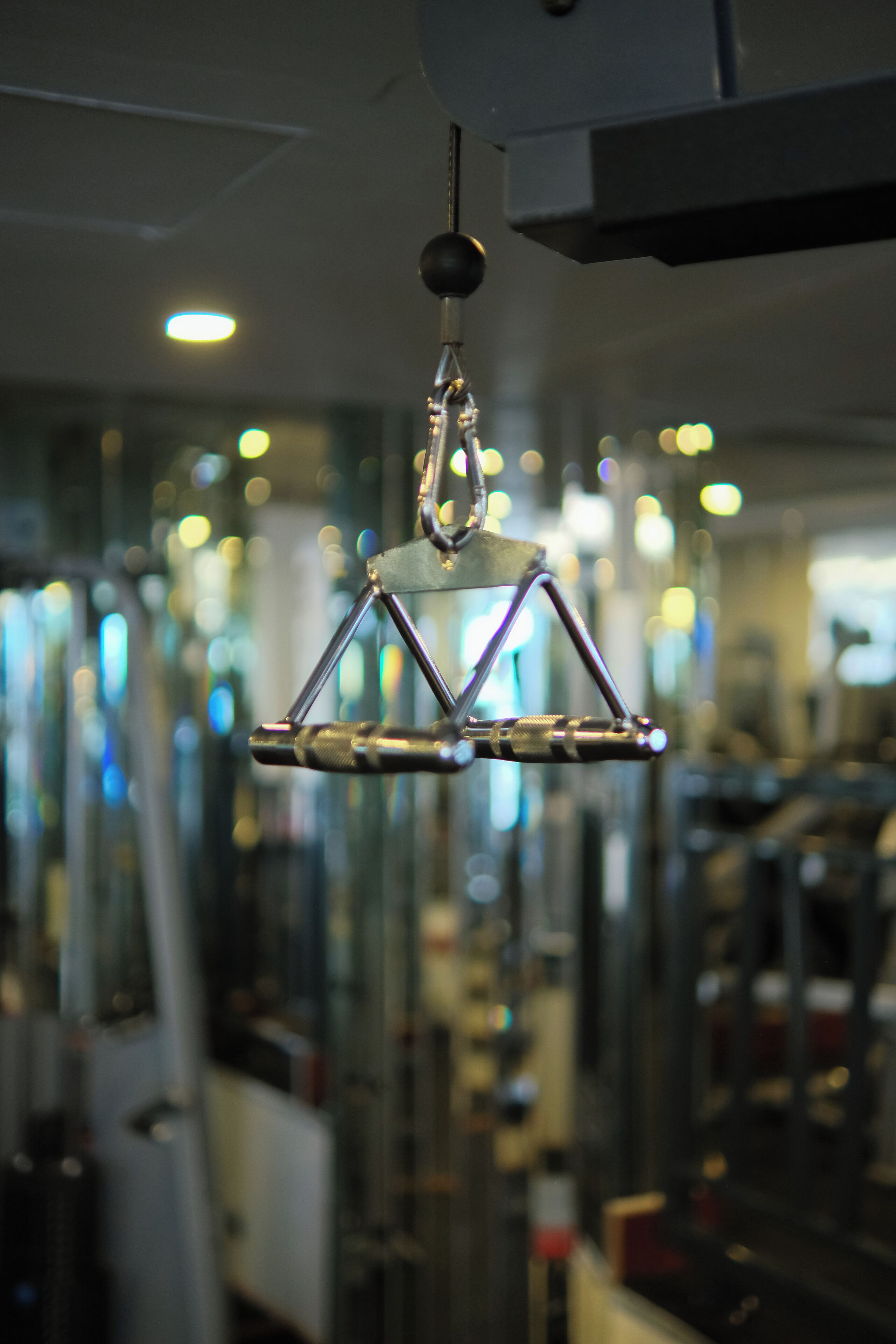 A hanging object with a triangular frame, suspended from a ceiling fixture in a room with glass partitions and reflective surfaces.