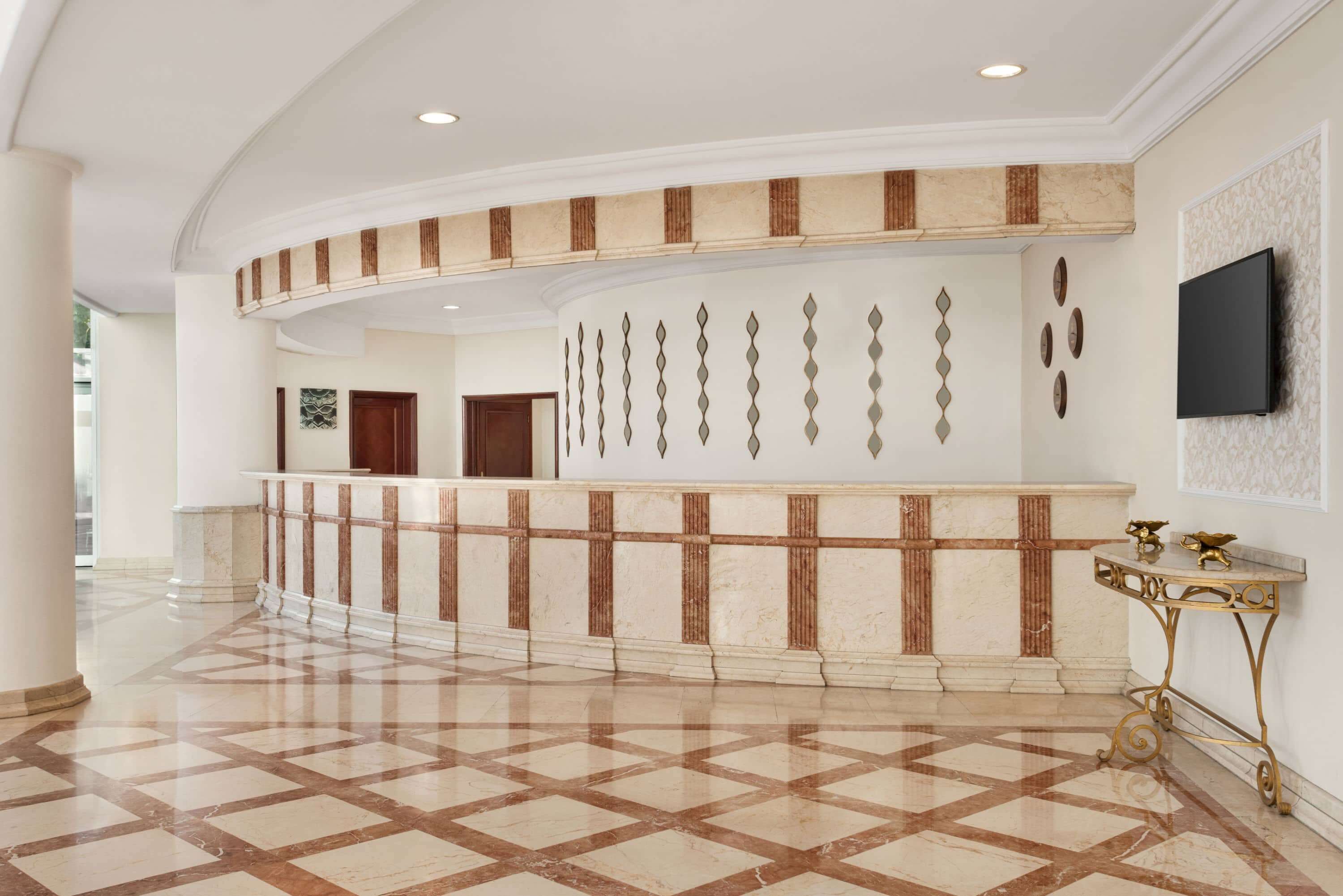 A lobby with a marble reception desk, a flat-screen TV mounted on the wall, and a patterned floor.