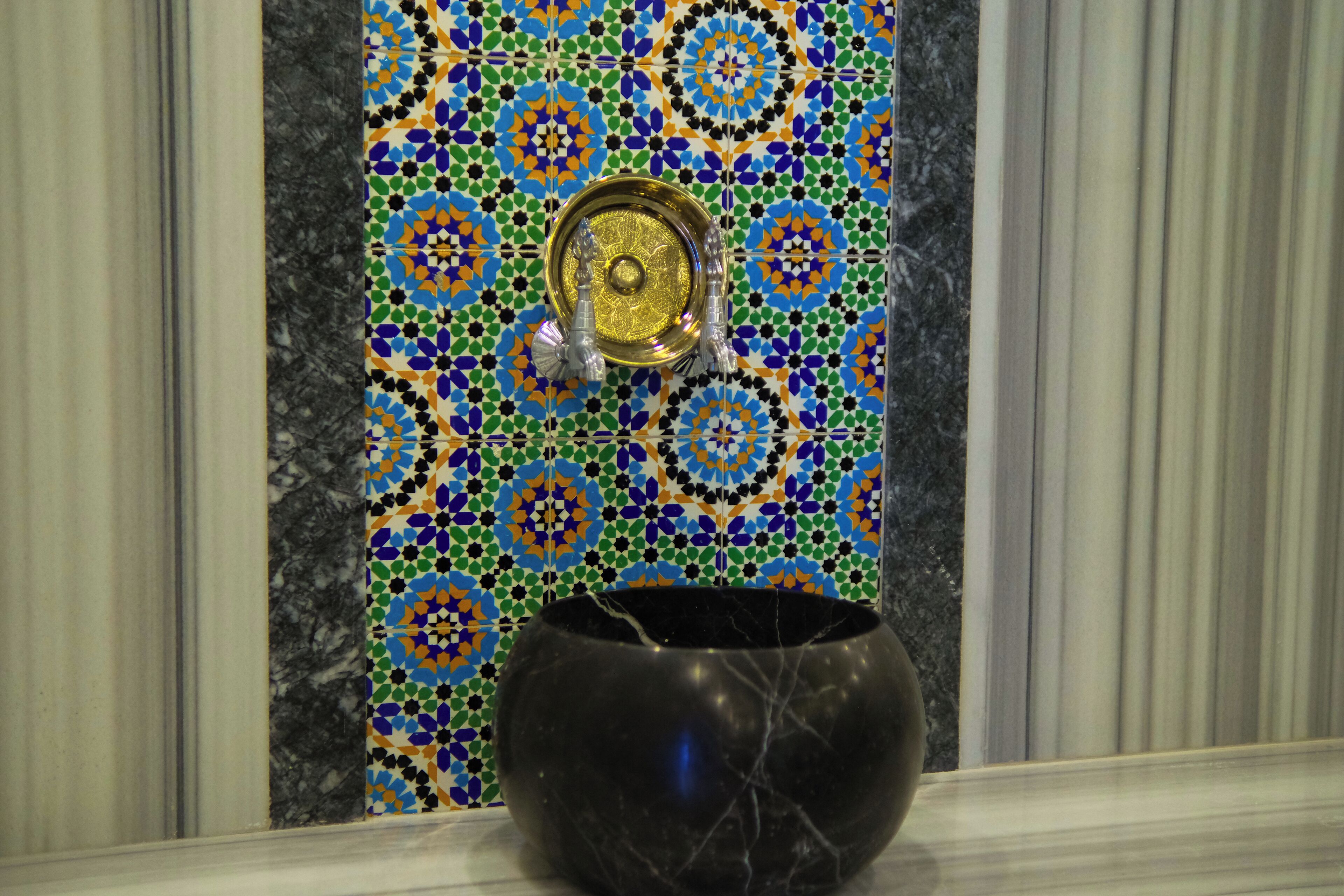 A black marble basin in a bathroom with a tiled wall featuring a geometric pattern.