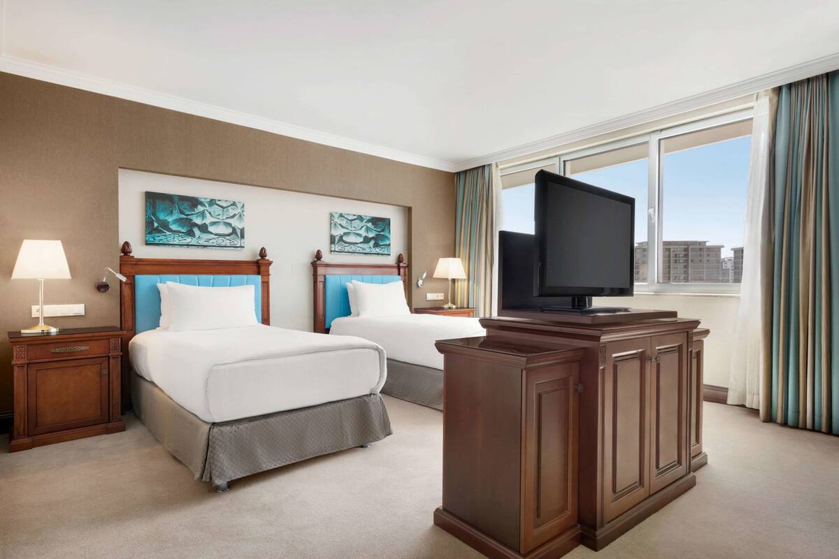 A hotel room with two beds, a television, and a large window with curtains.