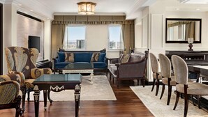 A spacious living room with a blue sofa, patterned armchairs, a glass coffee table, and a dining area with chairs and a table. - Wyndham Grand Kayseri (Kocasinan)