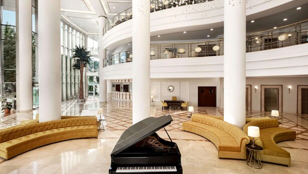A spacious lobby with a grand piano, curved sofas, and a high ceiling with decorative elements. - Wyndham Grand Kayseri (Kocasinan)