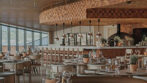 A restaurant with a curved wooden ceiling, a bar area with bottles and plants, and tables set for dining.