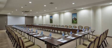 A conference room with long tables, chairs, water bottles, and a projector screen.