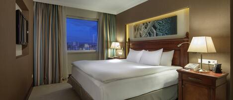 Une chambre d’hôtel avec un grand lit, deux tables de chevet avec des lampes, un téléviseur à écran plat et une fenêtre avec des rideaux.