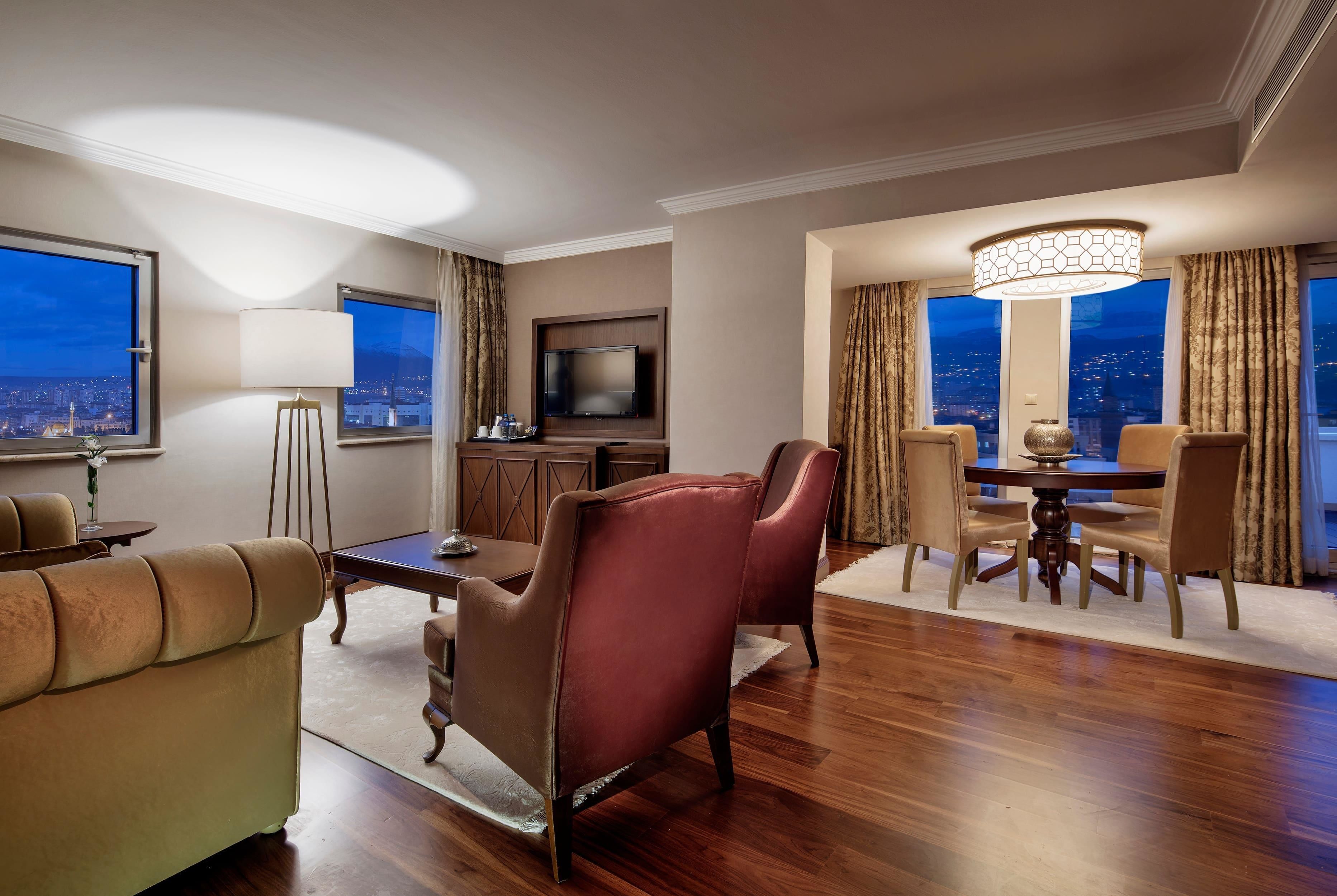 A hotel room with a city view, a dining area, and a TV.