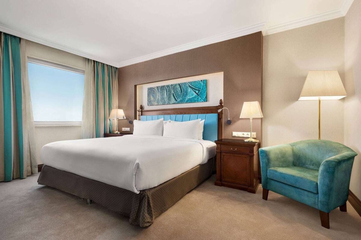 A hotel room with a large bed, a nightstand, a lamp, and a chair.