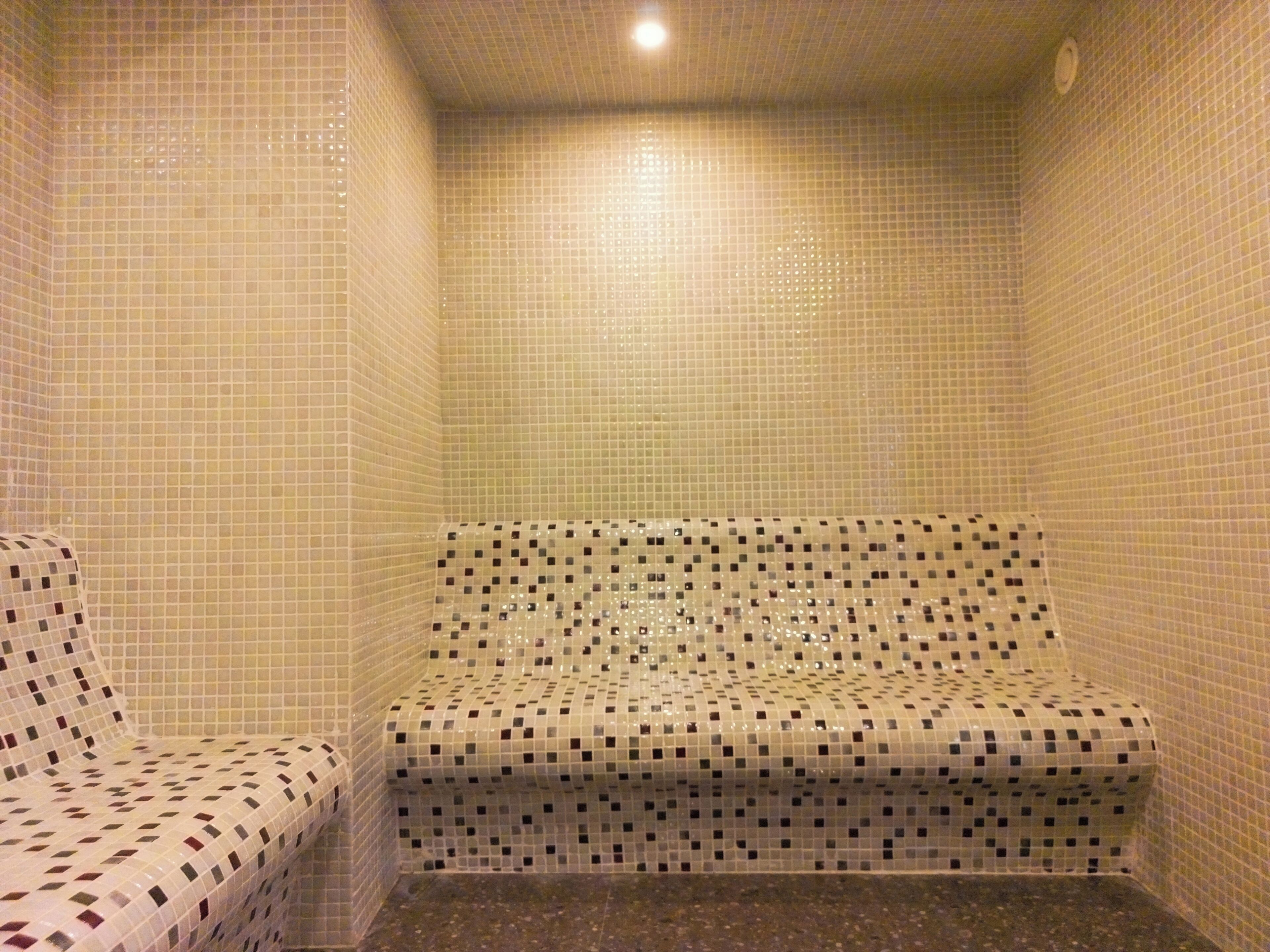 A small, tiled bathroom with a bench and a shower area.