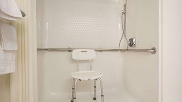 A bathroom with a shower, a white towel rack, and a white step stool.