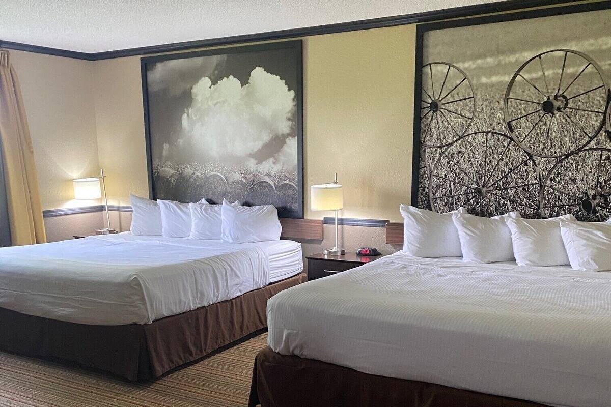 Ein Hotelzimmer mit zwei Betten, einem großen abstrakten Gemälde an der Wand und einem dekorativen Metall-Kopfteil.