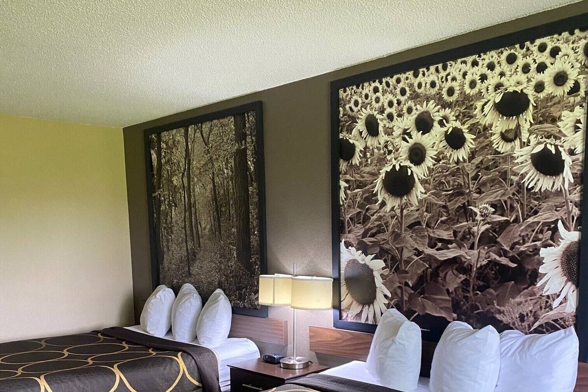 Ein Hotelzimmer mit einem großen Bett, zwei Nachttischen, einer Lampe und einer Wand mit einem Sonnenblumen-Wandbild.