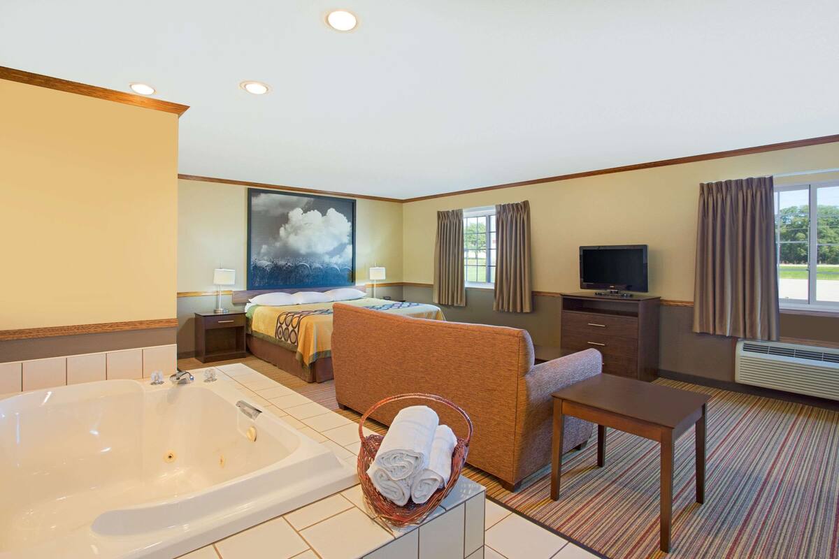 Ein Hotelzimmer mit einer großen Badewanne, einem Bett, einem Sofa, einem Fernseher und einem Fenster mit Vorhängen.