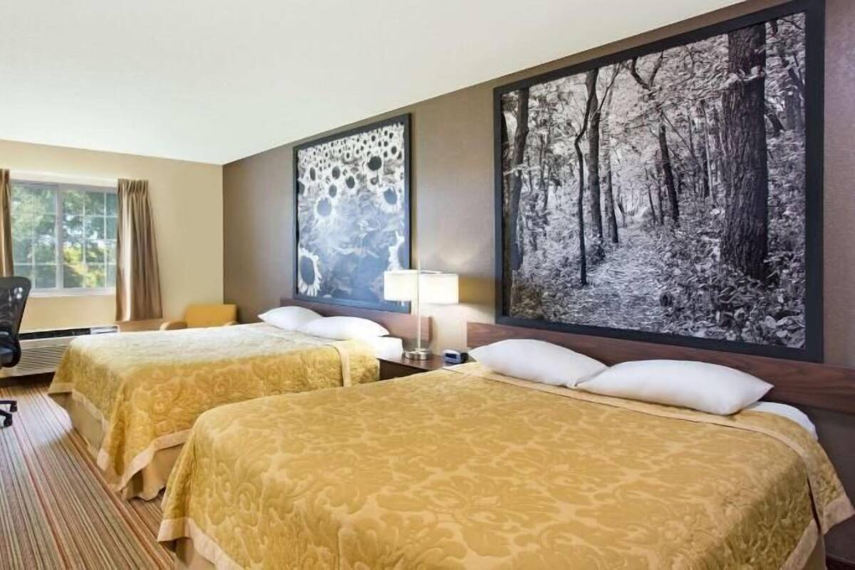 Ein Hotelzimmer mit zwei Betten, einem Schreibtisch mit Stuhl, einem Fernseher und einem großen Wandbild mit Waldmotiv.