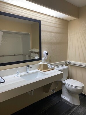 A hotel bathroom with a large mirror, a sink, a toilet, and a hand dryer. - Super 8 by Wyndham New Hampton (New Hampton)