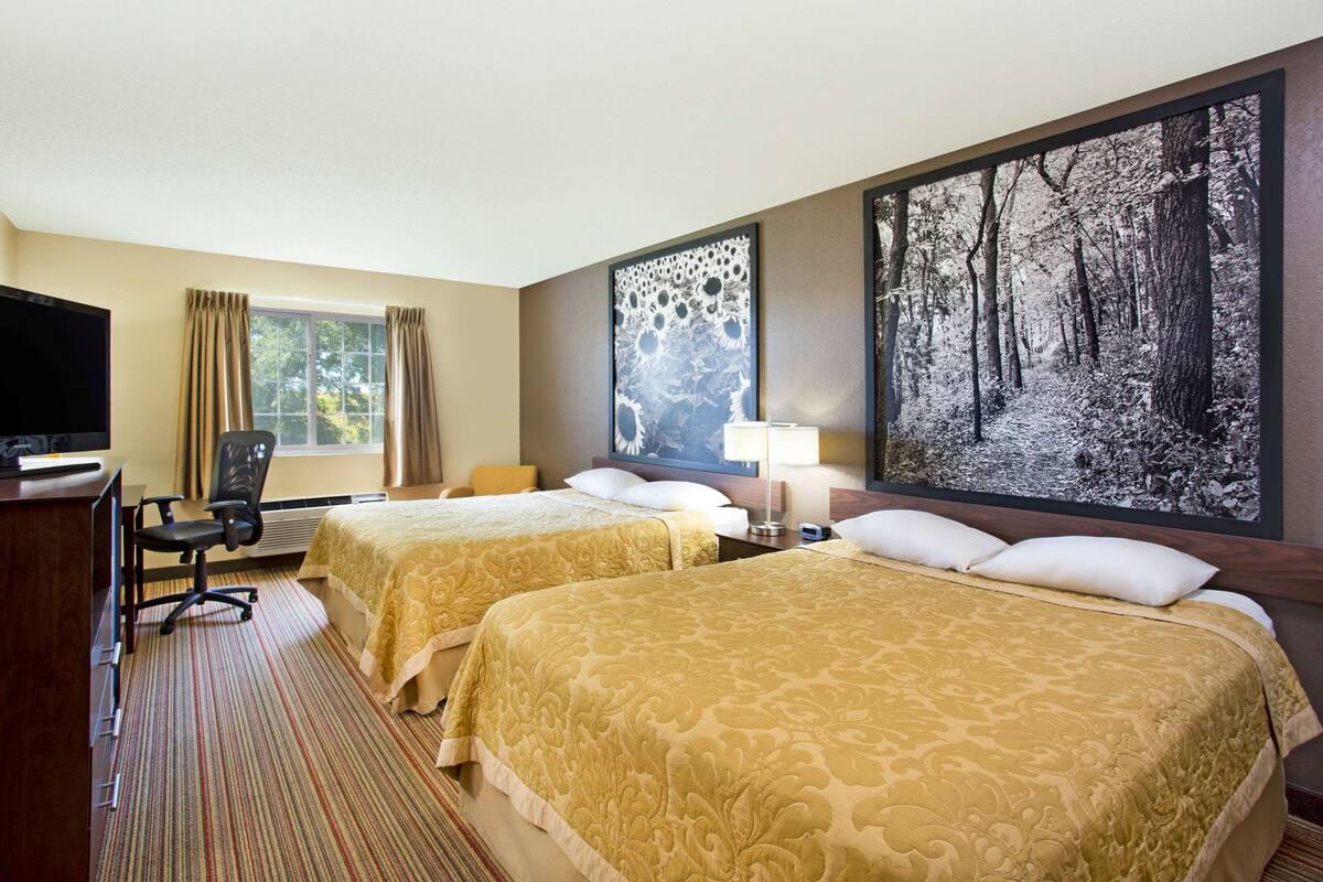 Ein Hotelzimmer mit zwei Betten, einem Schreibtisch, einem Sessel, einem Fernseher und einem großen Wandbild zum Thema Wald.