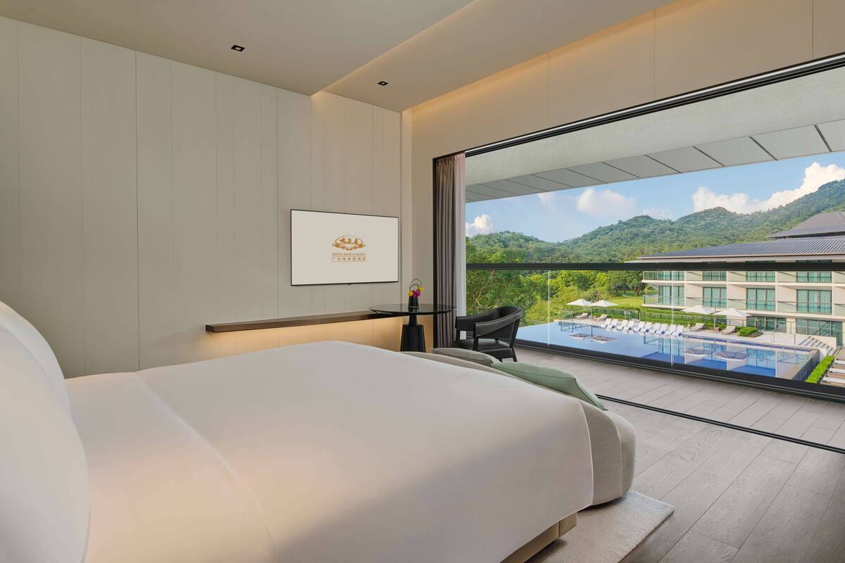 Une chambre d’hôtel moderne avec un grand lit, une petite table, une chaise et une vue sur une piscine et des montagnes.