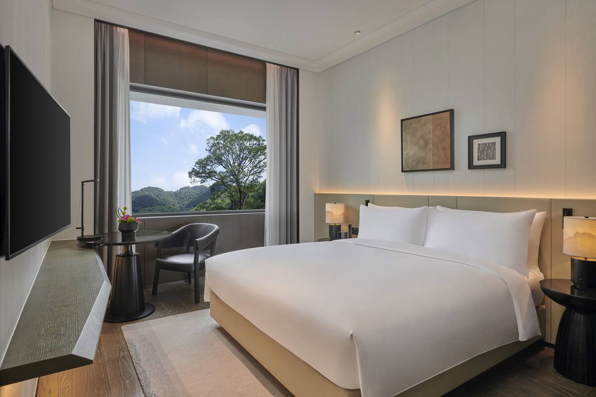 Une chambre d’hôtel moderne dotée d’un grand lit, d’une télévision à écran plat, d’une table à manger et offrant une vue sur les montagnes.