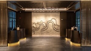 Un área de recepción con diseño moderno, que presenta una pared central con un motivo decorativo, dos mostradores de recepción y un techo con iluminación lineal.
