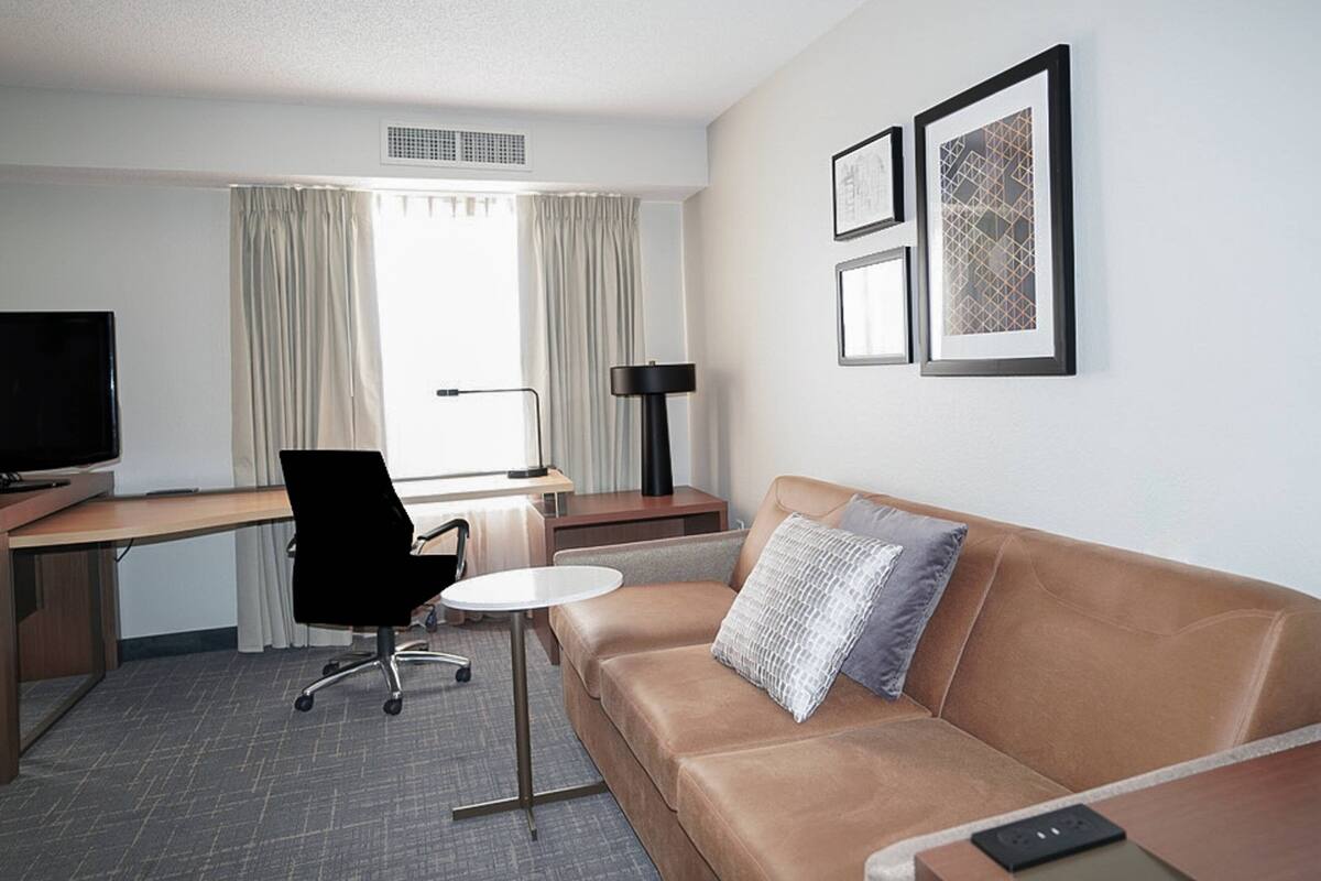 A hotel room with a bed, a desk, a chair, a TV, and framed pictures on the wall.
