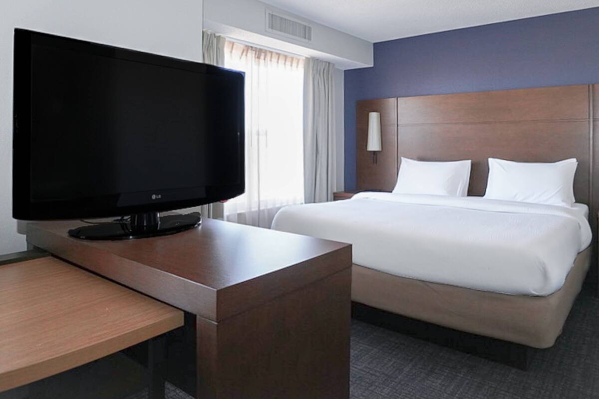 A hotel room with a bed, a flat-screen TV, a wooden desk, and a nightstand.