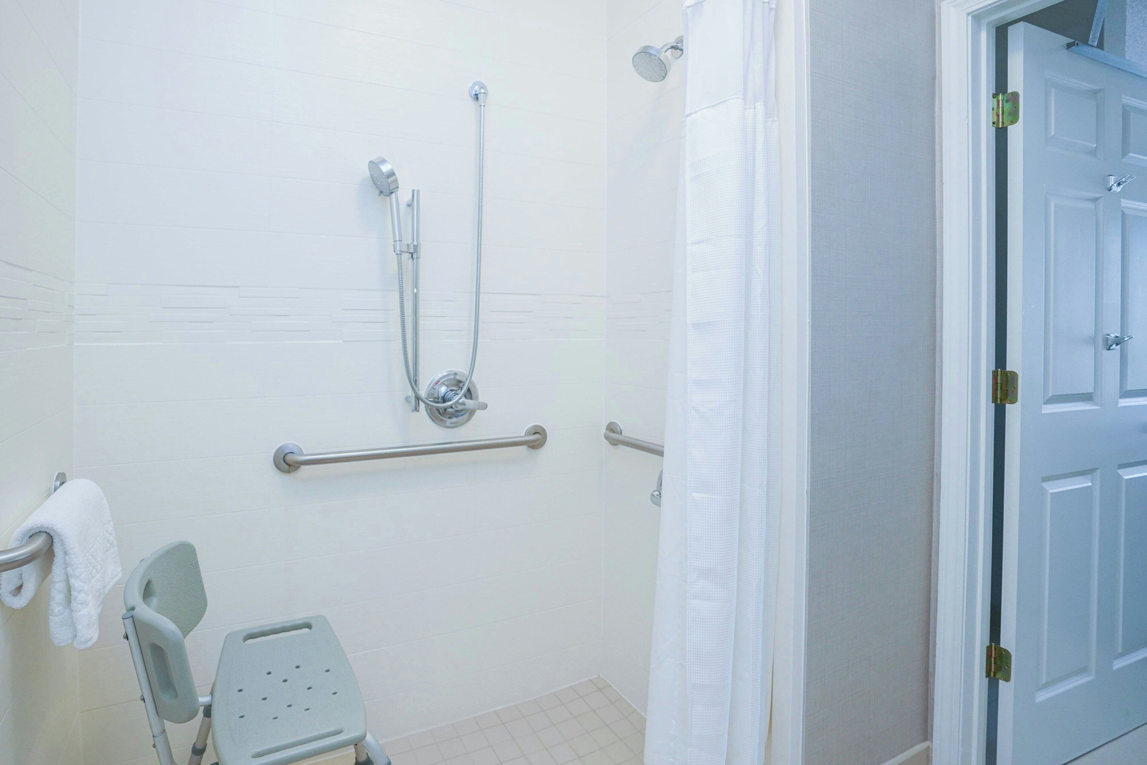 Une salle de bain équipée d’une douche, de barres d’appui, d’un porte-serviettes et d’une porte.
