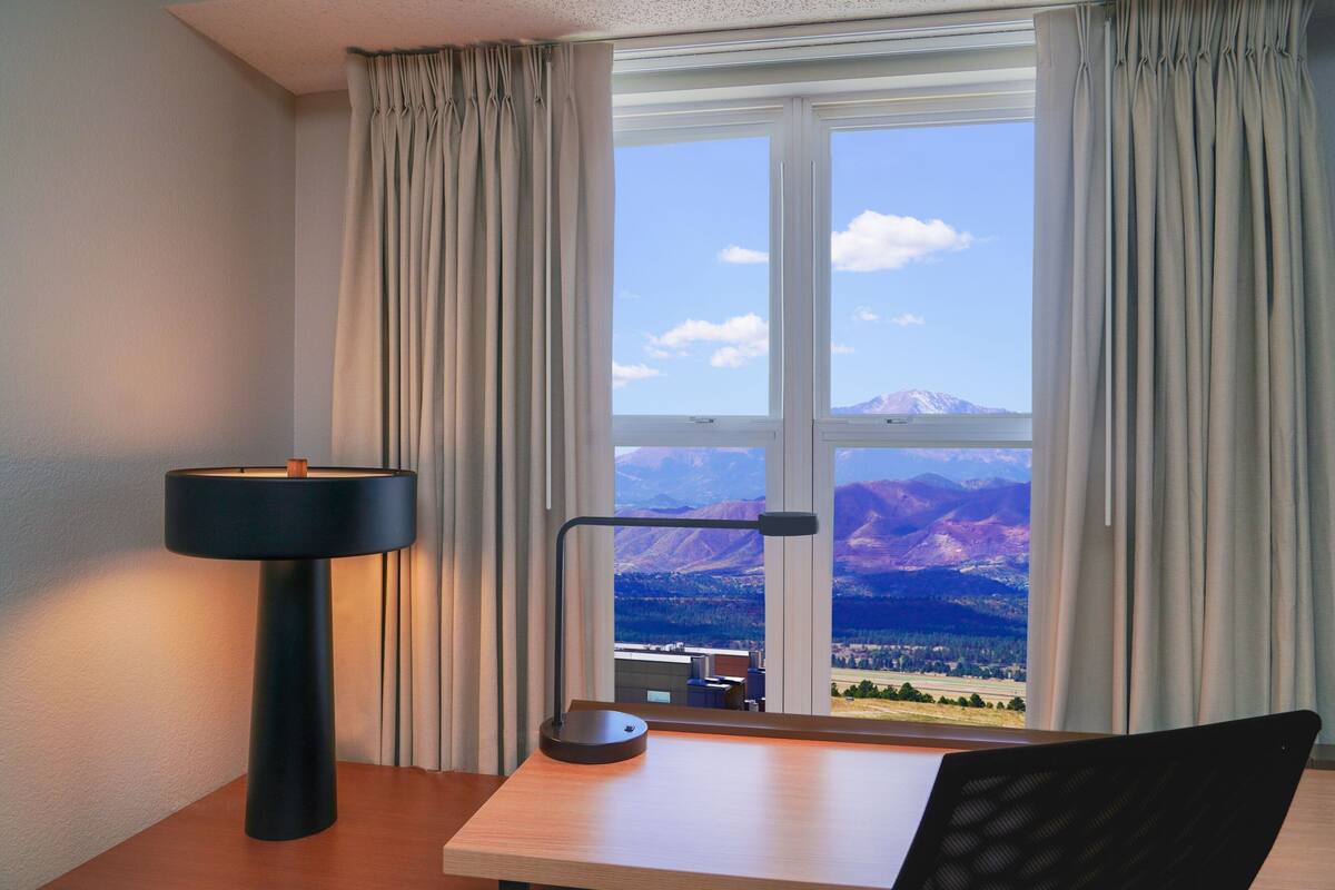 A room with a desk, a lamp, and a view of mountains through a window.