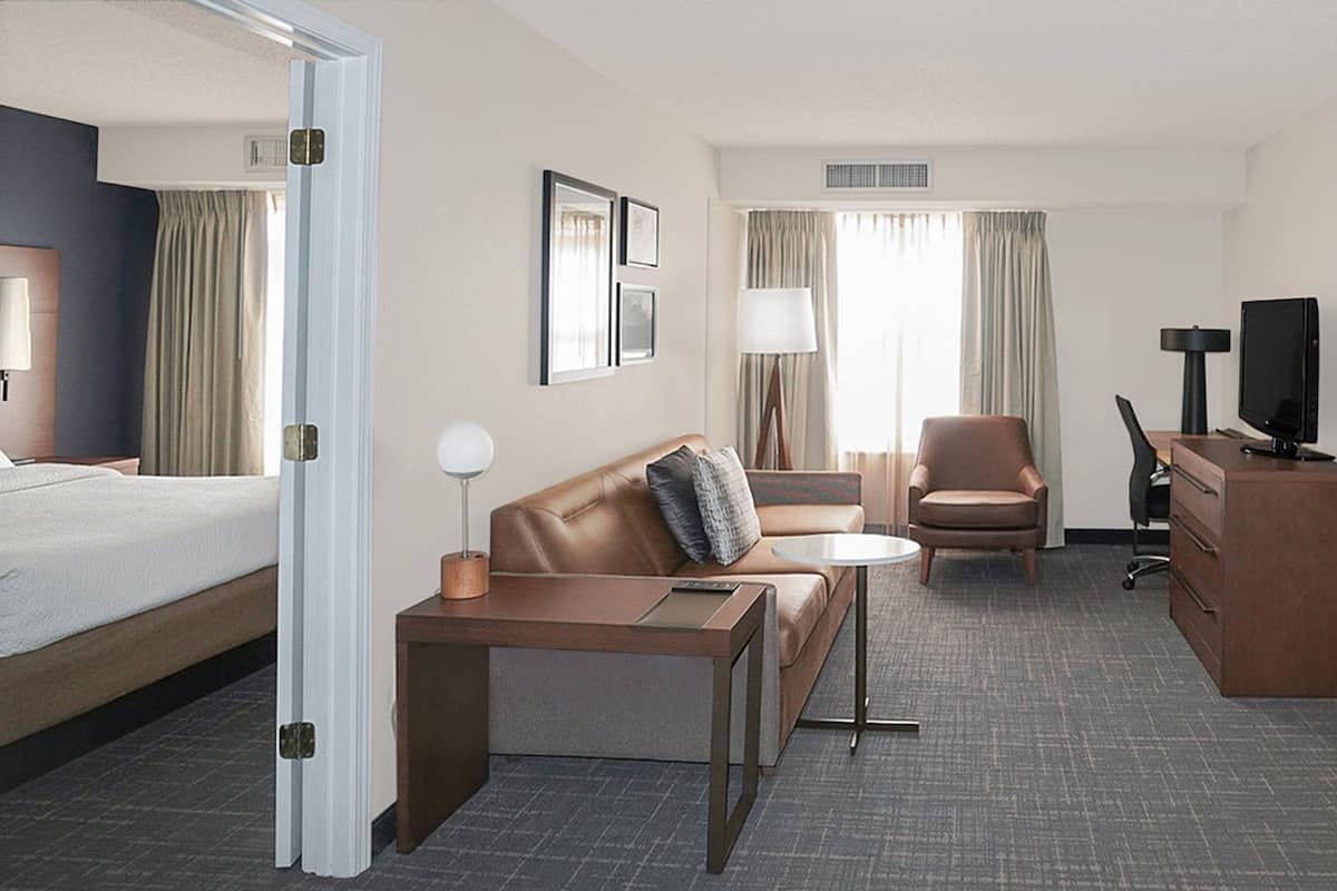 A hotel room with a bed, a sofa, a desk, a chair, a TV, and a lamp.