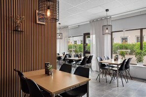 A modern dining area with wooden paneling, black chairs, and pendant lighting.