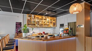 Un espace bar avec un comptoir en bois, des étagères remplies de bouteilles, une plante en pot et un luminaire suspendu.