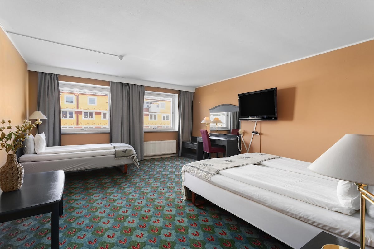Ein Hotelzimmer mit zwei Betten, einem Schreibtisch, einem Stuhl, einem Fernseher und einem Fenster mit Vorhängen.
