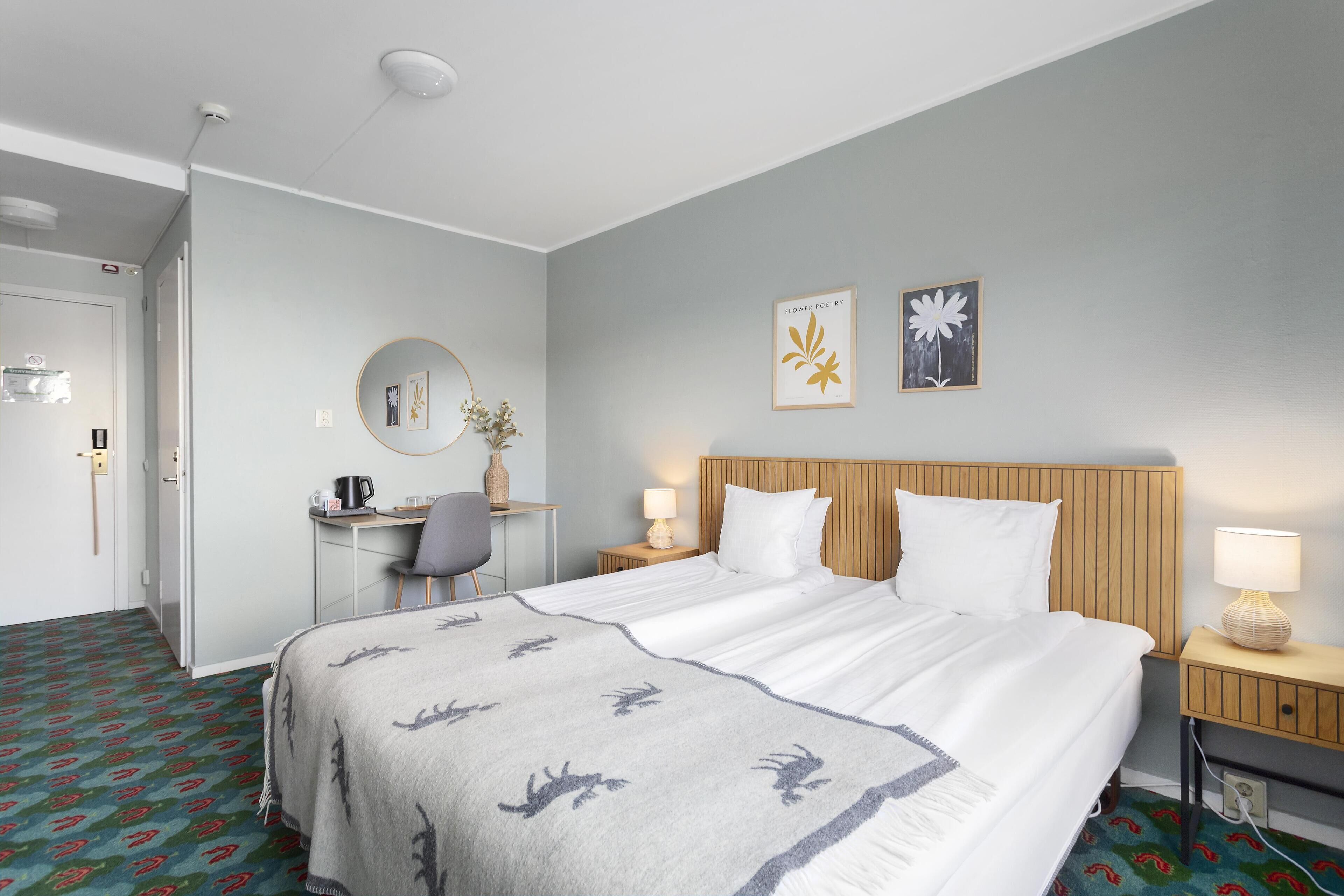Ein Hotelzimmer mit Bett, Schreibtisch, Stuhl und einem kleinen Tisch mit Lampe.