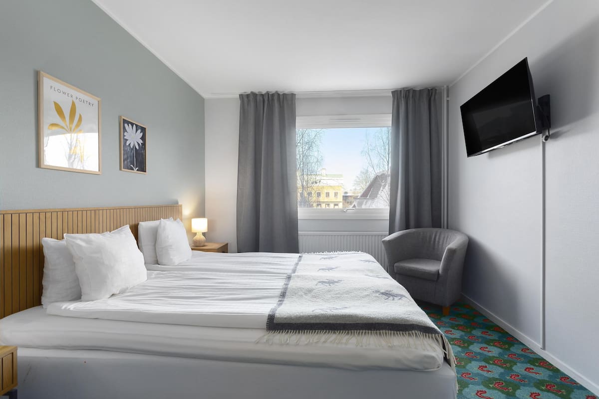 Ein Hotelzimmer mit Bett, Sessel, Fernseher und einem Fenster mit Vorhängen.
