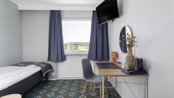 Een hotelkamer met een bed, een bureau met stoel, een televisie, een spiegel en een raam met gordijnen.