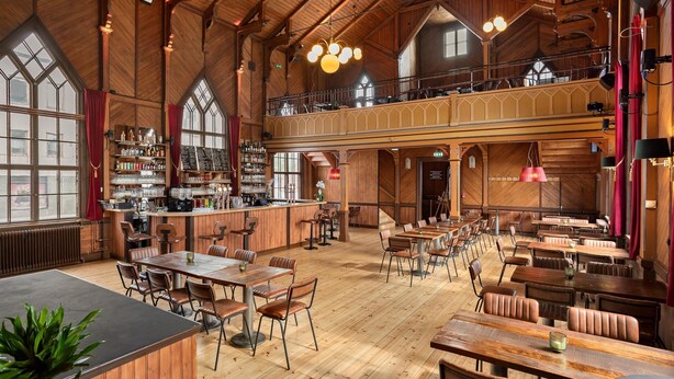 Un intérieur spacieux en bois, avec plusieurs tables et chaises, un coin bar et de grandes fenêtres.