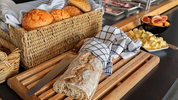 Una tabla de madera con una hogaza de pan, una cesta de bollos y un cuenco de cubos de queso.