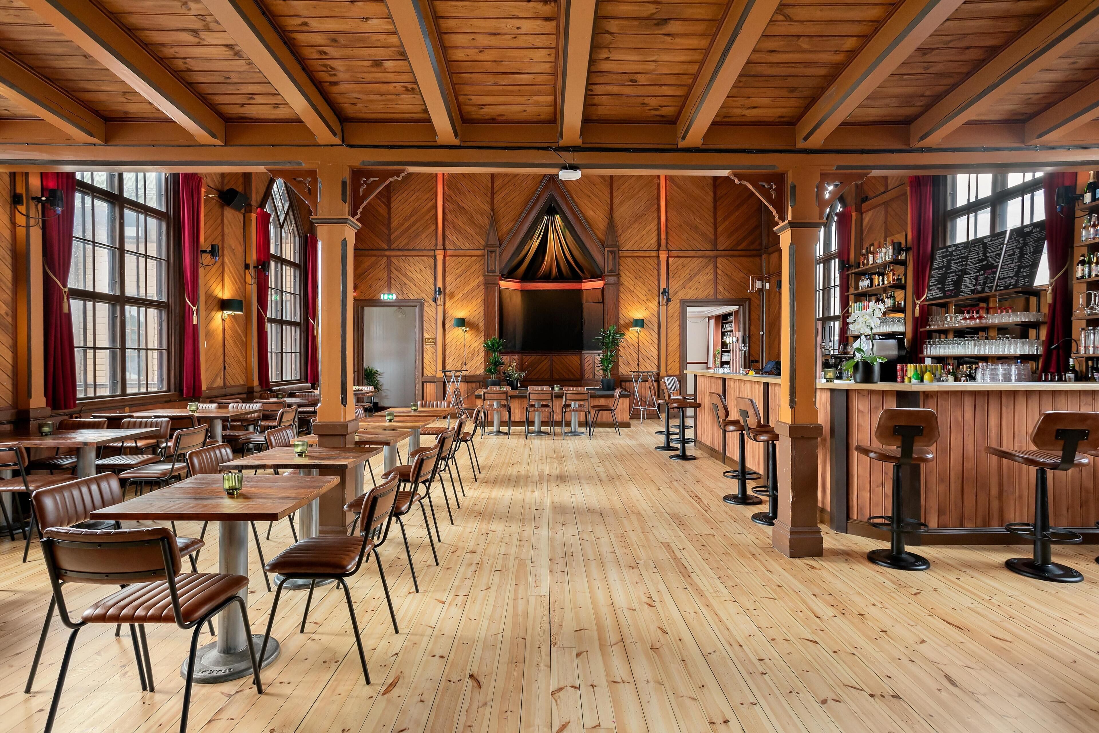 A restaurant with wooden floors, high ceilings, and a bar area.