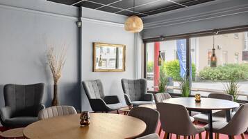 Un interior moderno con sillones tapizados en gris, una mesa redonda de madera y un gran ventanal con vista a la calle.