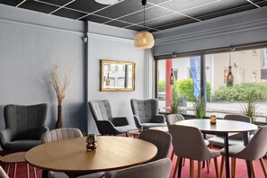 A modern interior with grey upholstered chairs, a round wooden table, and a large window with a view of the street.