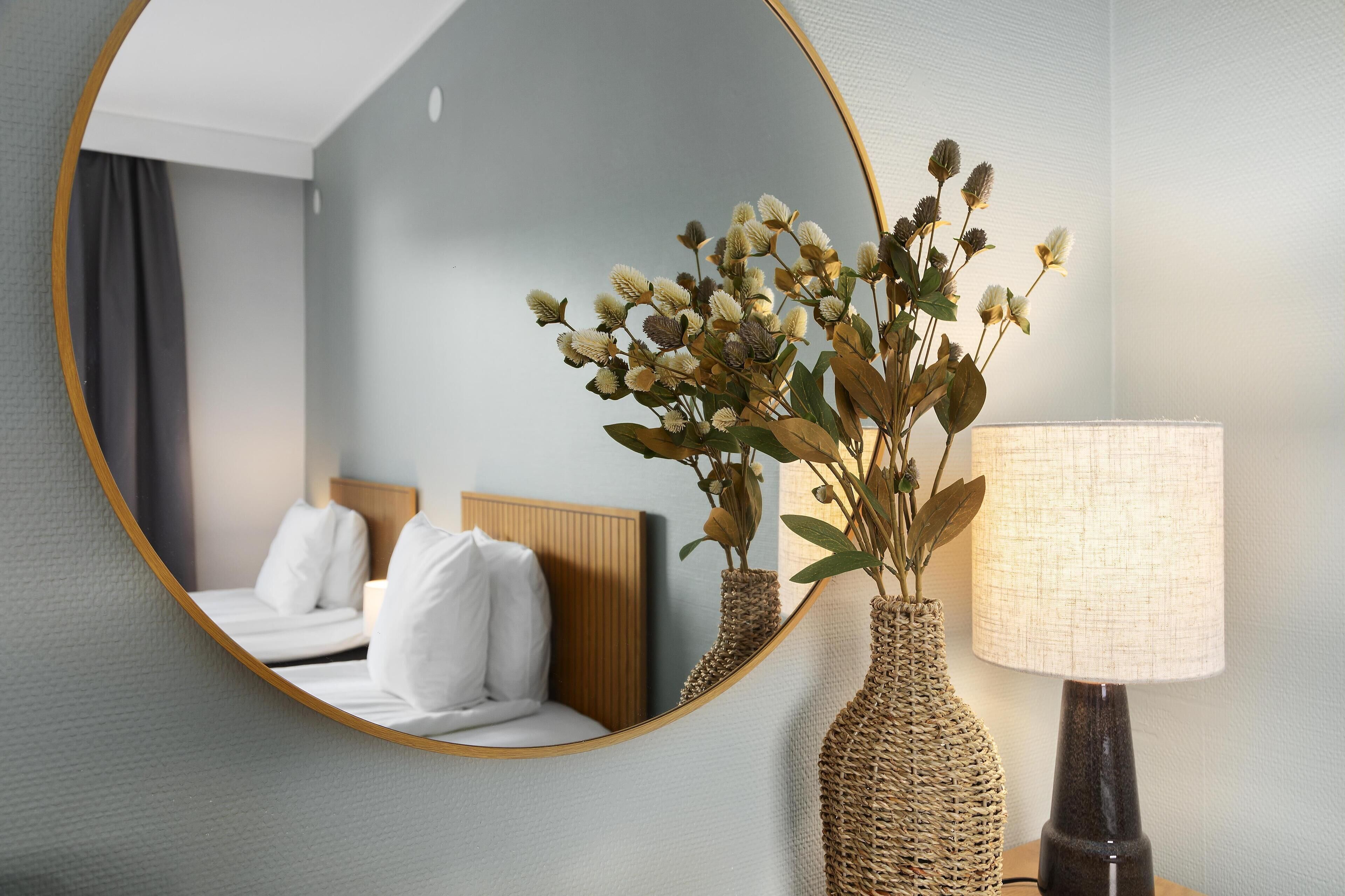 Una habitación de hotel con una cama, un espejo y una lámpara.