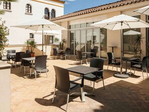Relax on the patio surrounded by lush greenery and enjoy the view of the adjacent building's interior.