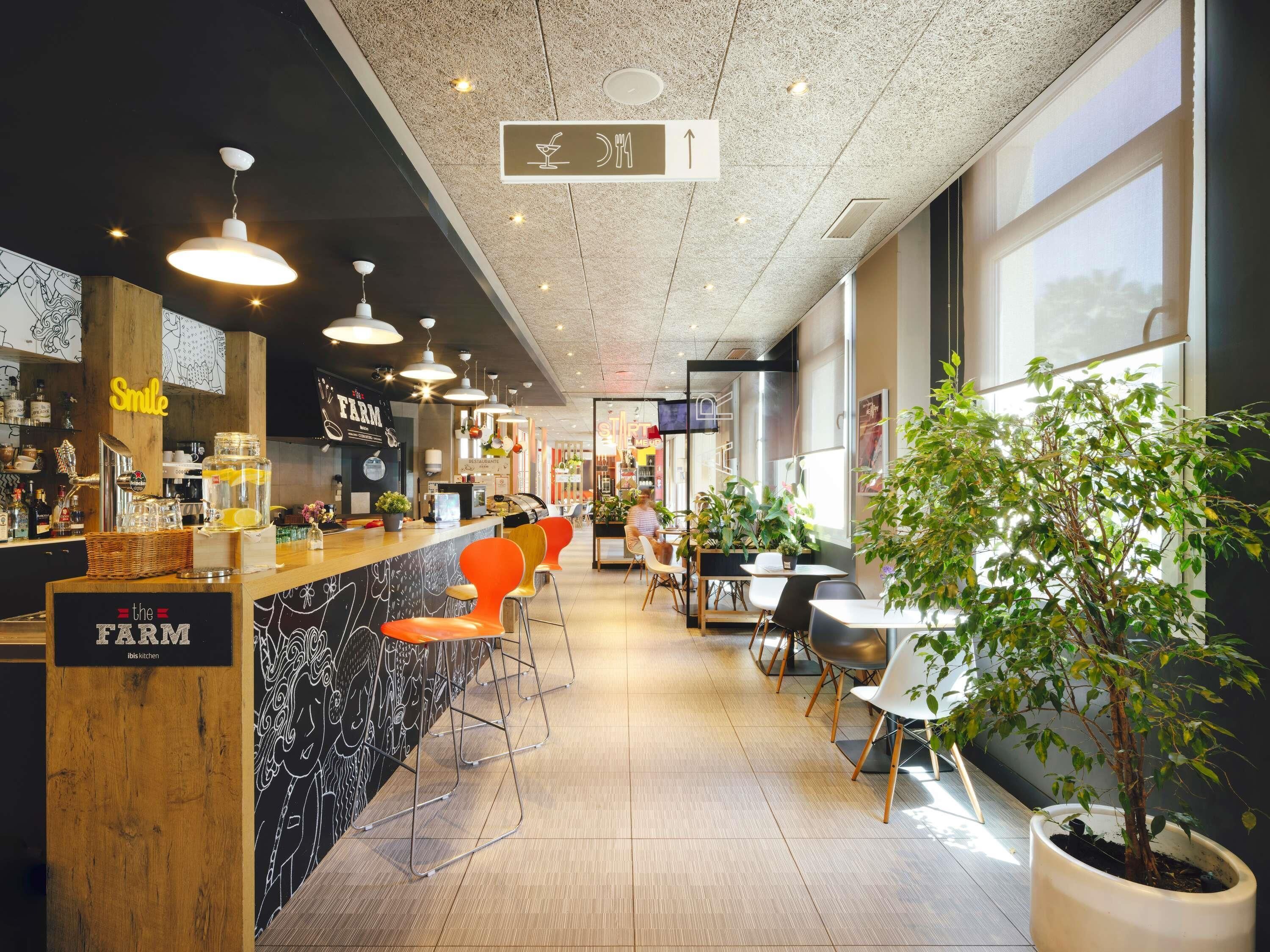 Interior de restaurante con barra, asientos y una planta en maceta.