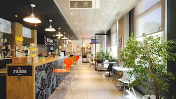 Interior de restaurante con barra, asientos y una planta en maceta.