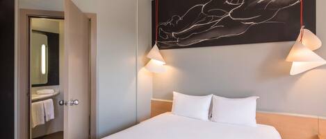Una habitación de hotel con una cama grande, una obra de arte colgada en la pared y dos lámparas colgantes.
