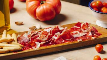 Una tabla de madera con carne curada en rodajas y un tazón de tomates cherry.